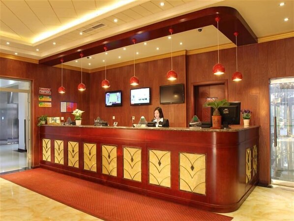A hotel reception area with a wooden reception desk, multiple pendant lights, and a flat-screen TV mounted on the wall.