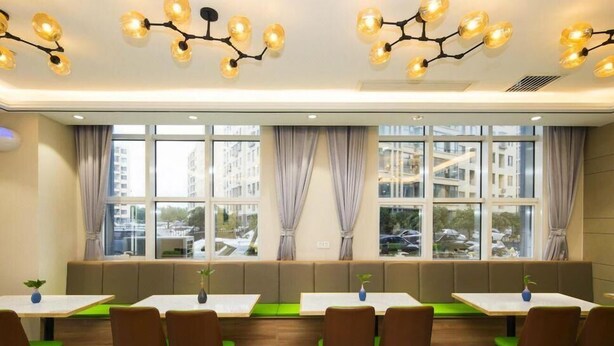 A restaurant with multiple tables and booths, large windows with curtains, and a modern chandelier. - GreenTree Inn Tianjin Xiqing Development Zone Renrenle Square Express Hotel (Tianjin)