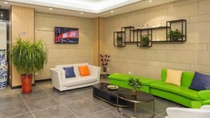 A modern lobby with a white sofa, a green sofa, a coffee table, and a large potted plant. - GreenTree Inn Tianjin Xiqing Development Zone Renrenle Square Express Hotel (Tianjin)