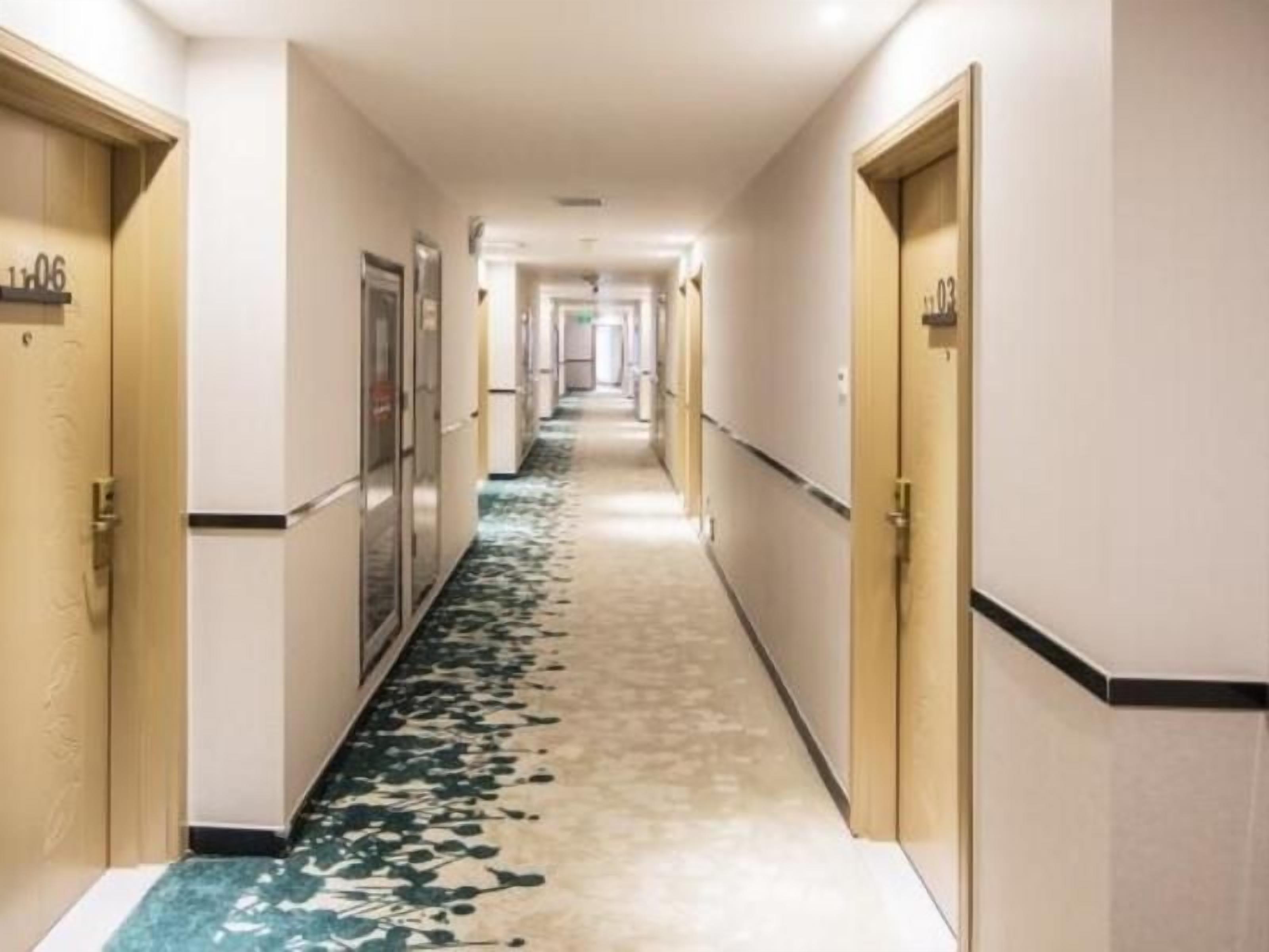 Un couloir d’hôtel avec des portes numérotées 106 et 103, un sol recouvert de moquette et un passage menant à un espace commun.