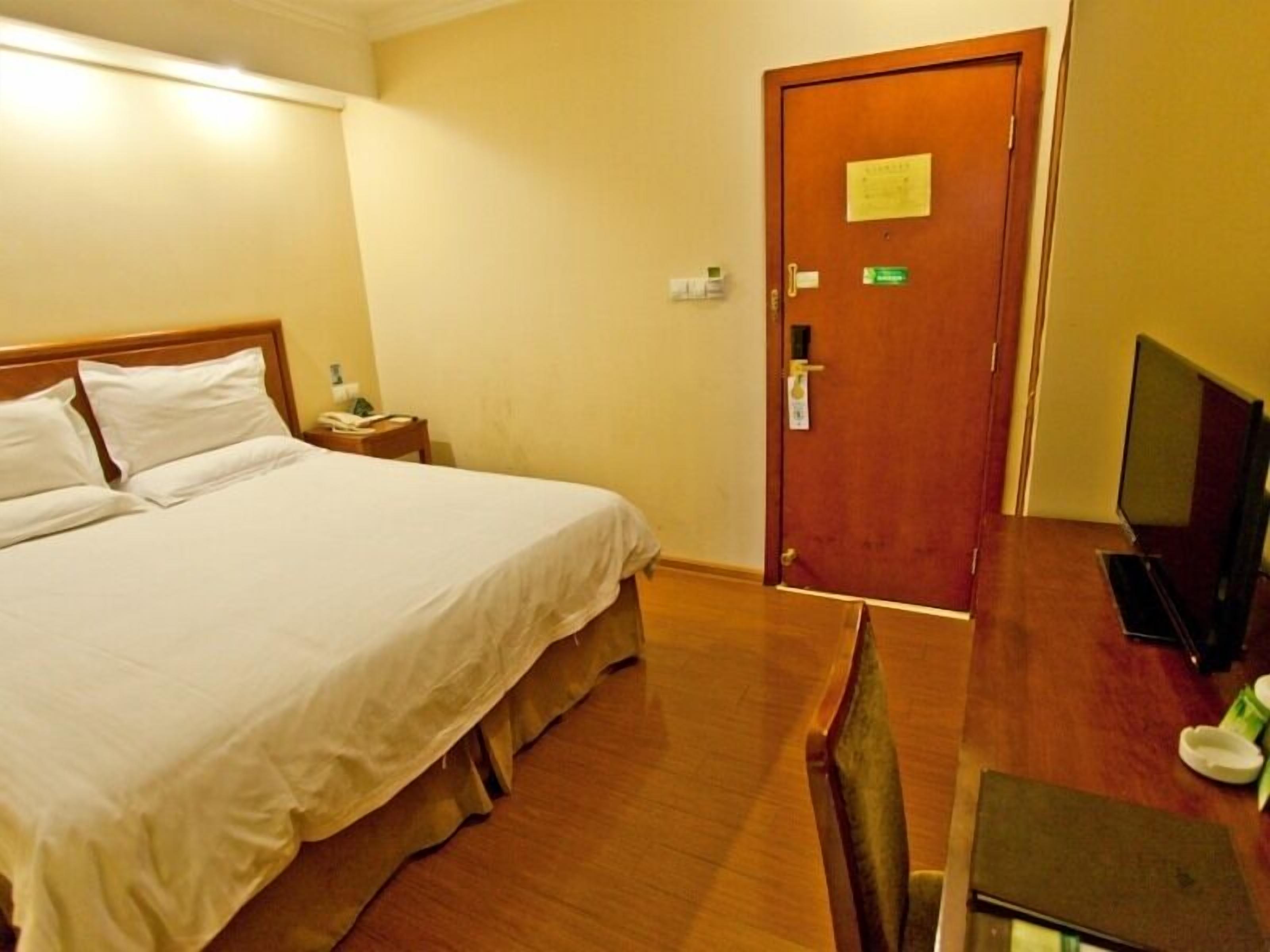 A hotel room with a bed, bedside table, TV, and a wooden desk.