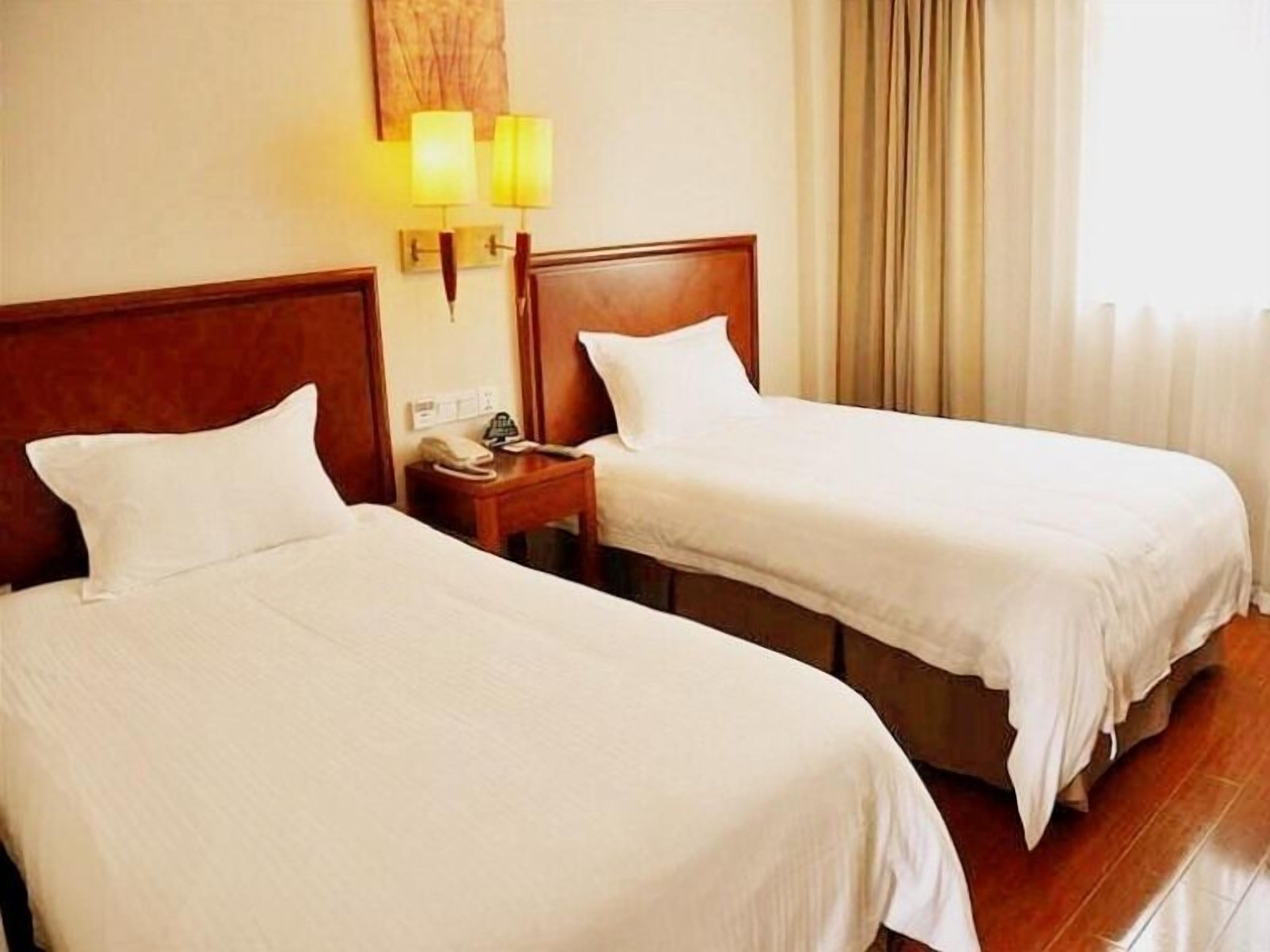Two single beds with wooden headboards, a bedside table with a lamp, and a window with curtains.