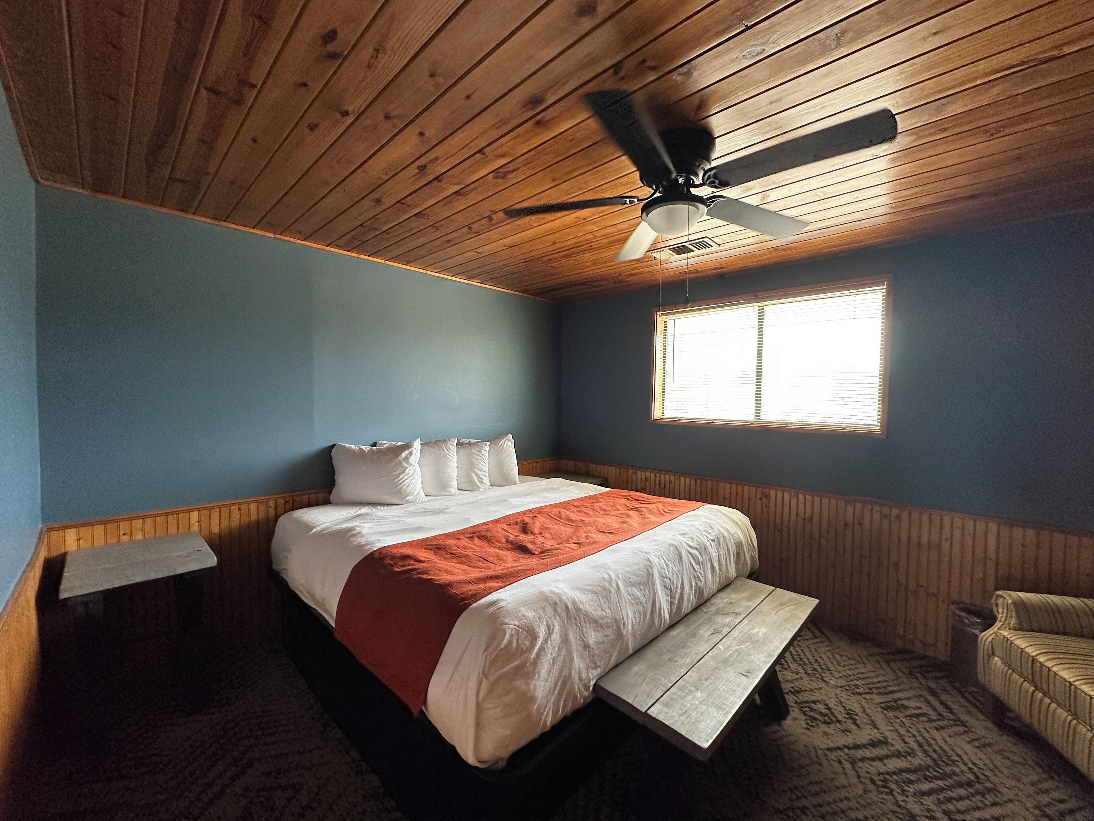 A bedroom with a bed, a wooden bench, a window, and a ceiling fan.