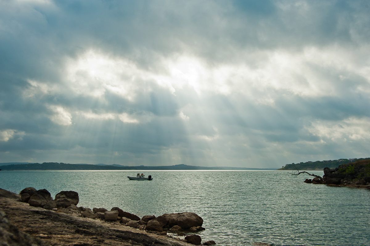 Et roligt hav med en båd i det fjerne, en stenet kystlinje og en overskyet himmel.