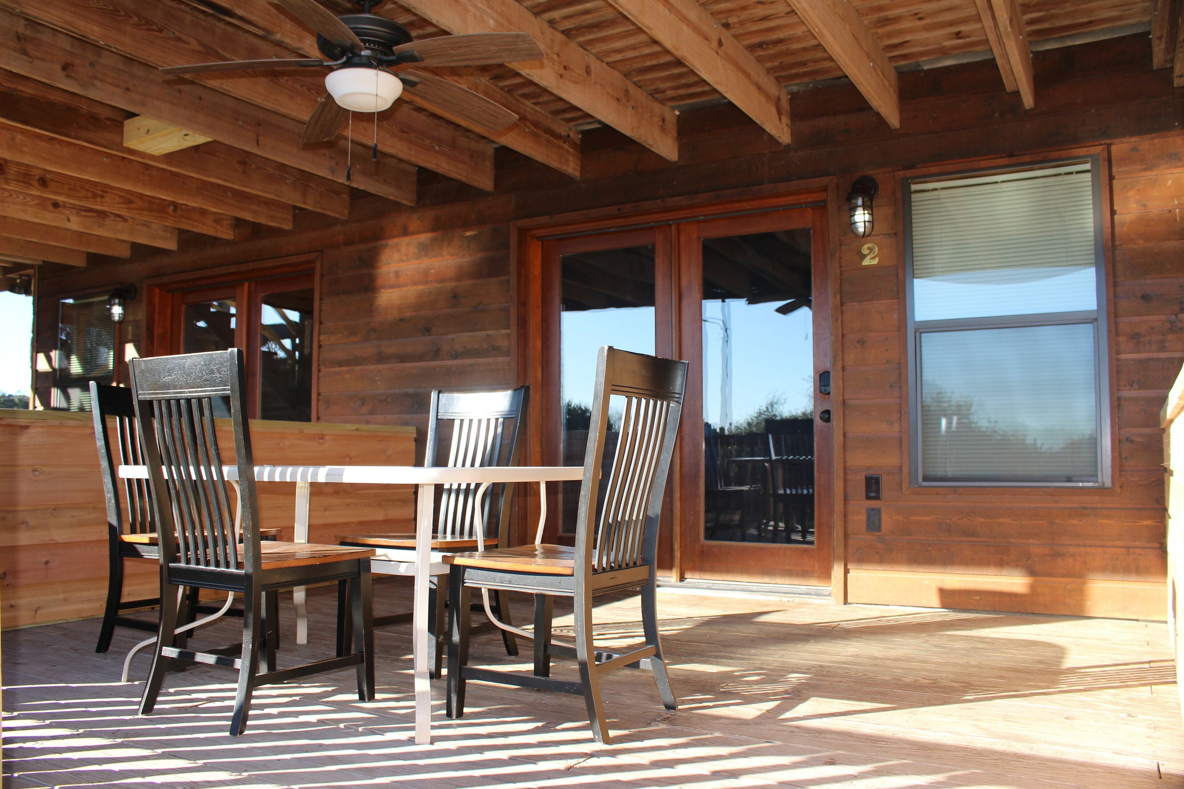 A wooden deck with a table and chairs, a ceiling fan, and a sliding glass door.