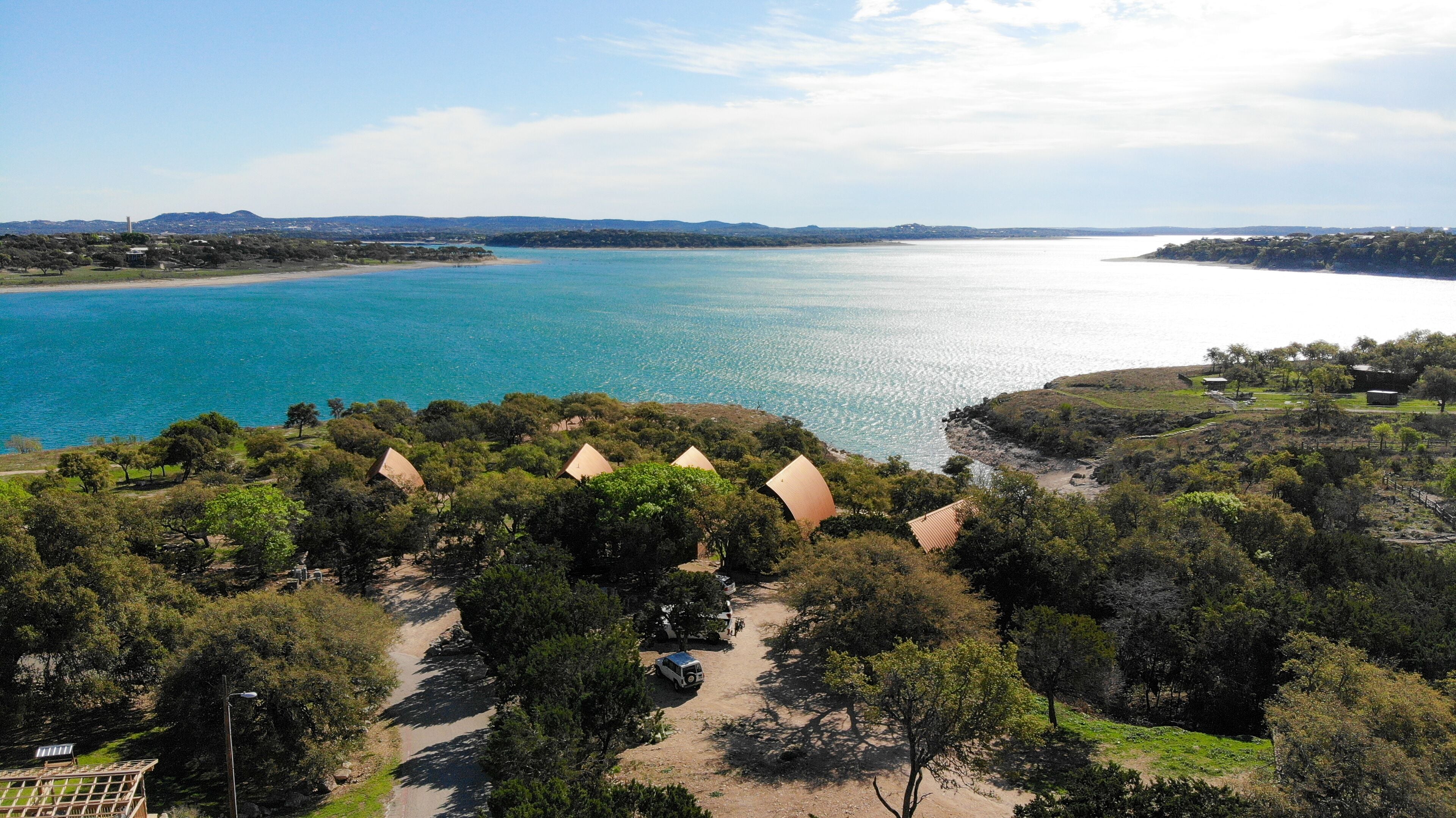 Zona costera con varias cabañas de techo de paja rodeadas de vegetación exuberante, vista despejada del mar y un paisaje urbano distante.