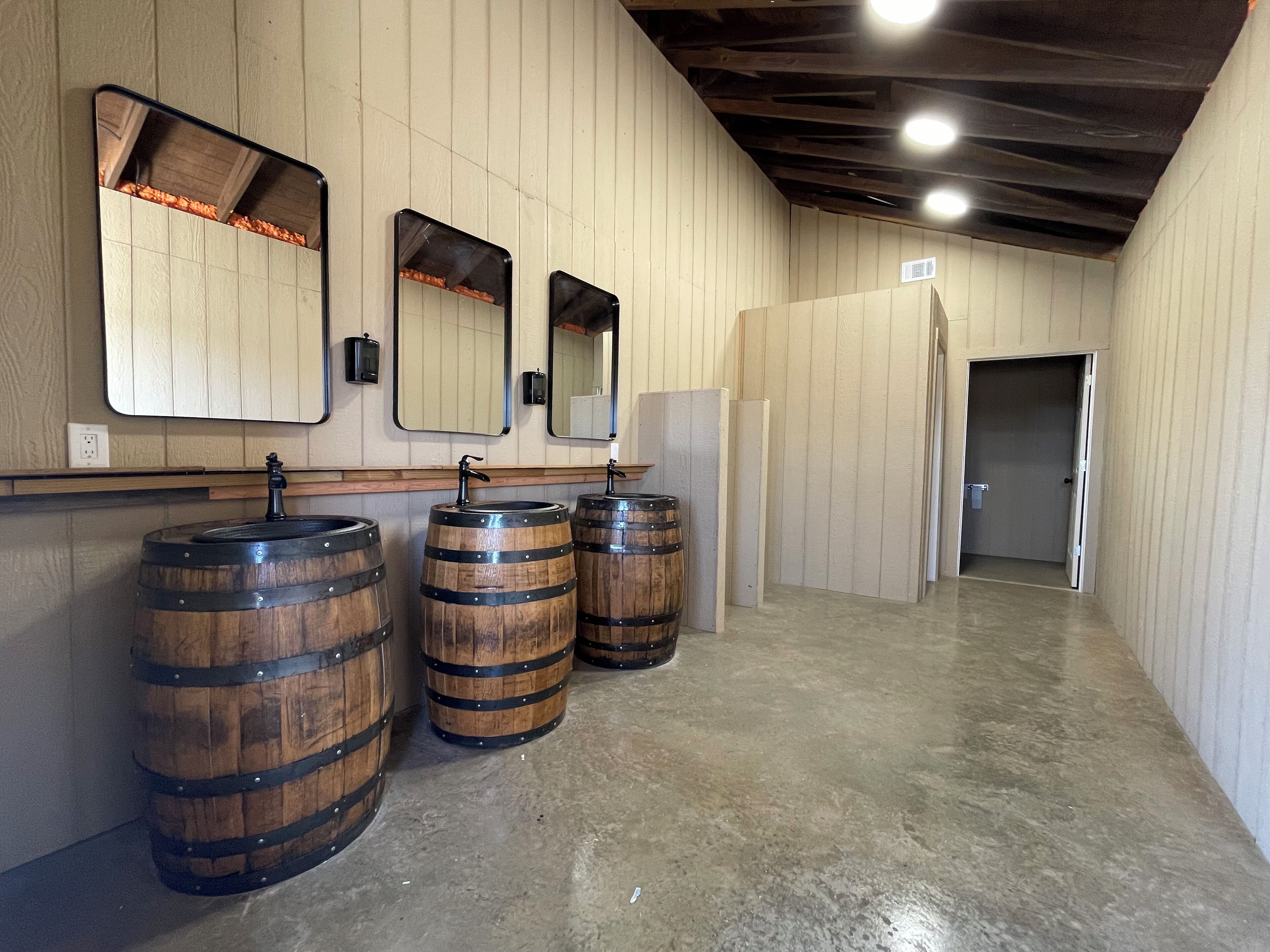 A restroom with wooden barrel sinks, mirrors, and a wooden ceiling.