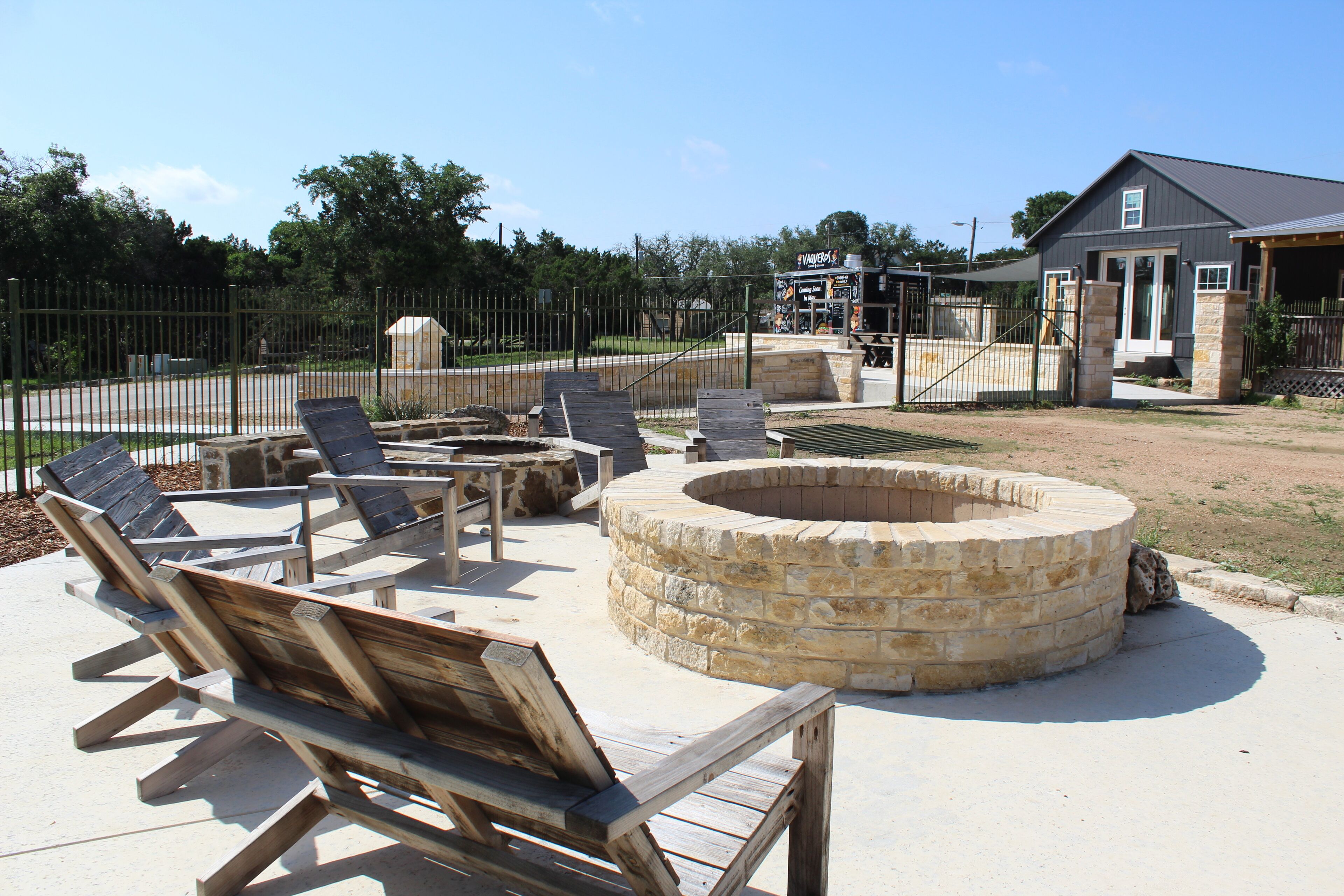 A patio area with wooden lounge chairs, a stone fire pit, and a fenced enclosure.