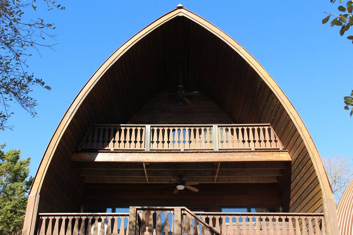 A wooden cabin with a triangular roof, a balcony on the upper level, and a ceiling fan.