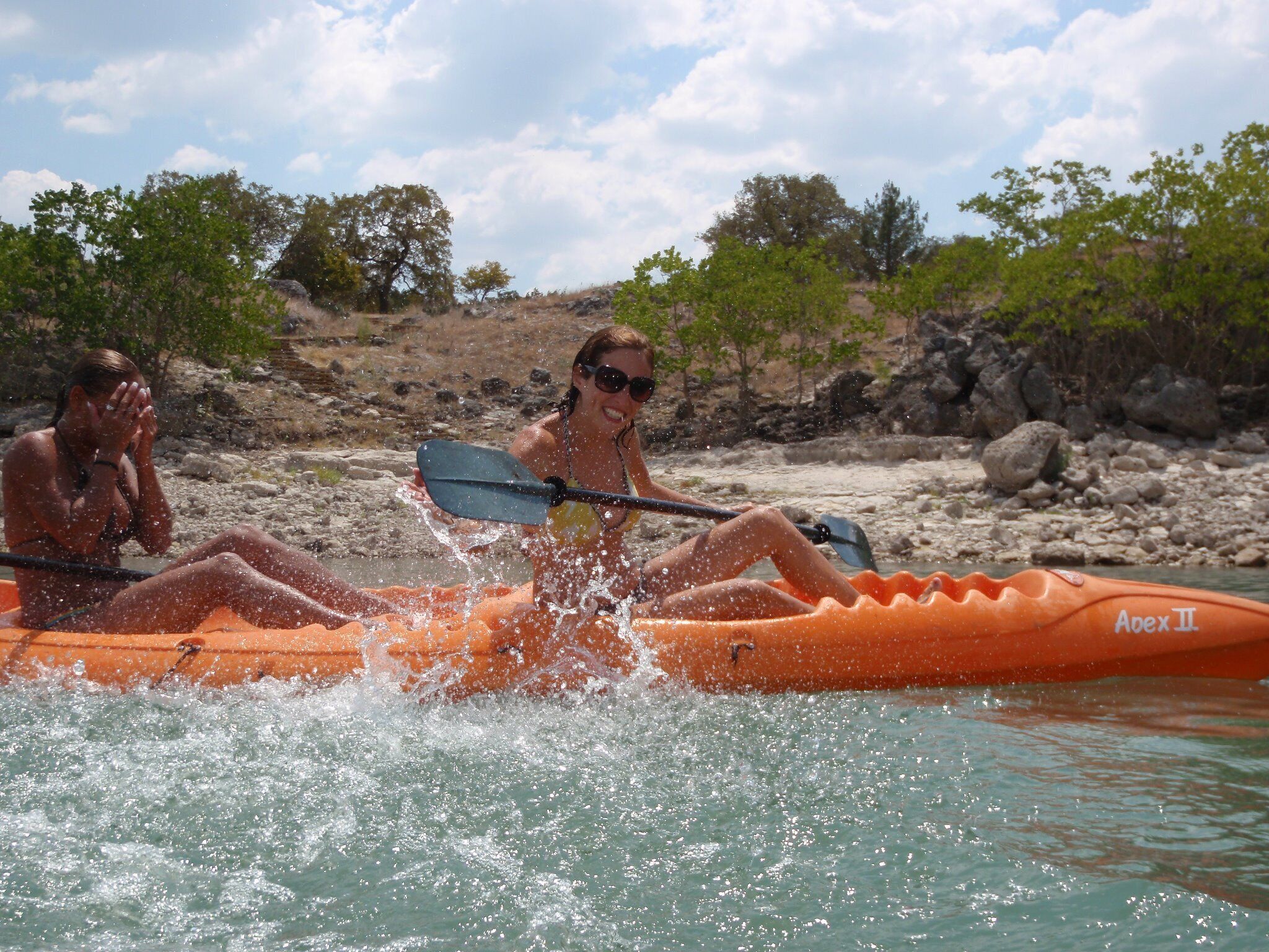 Two people kayaking in an orange raft with the brand name Apex II visible.