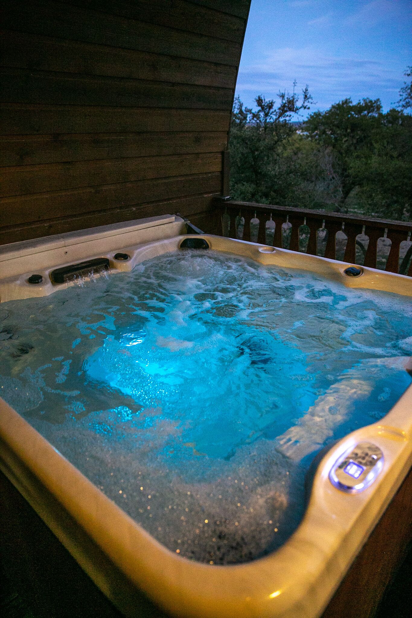 A hot tub with a digital control panel, surrounded by a wooden deck and a railing.