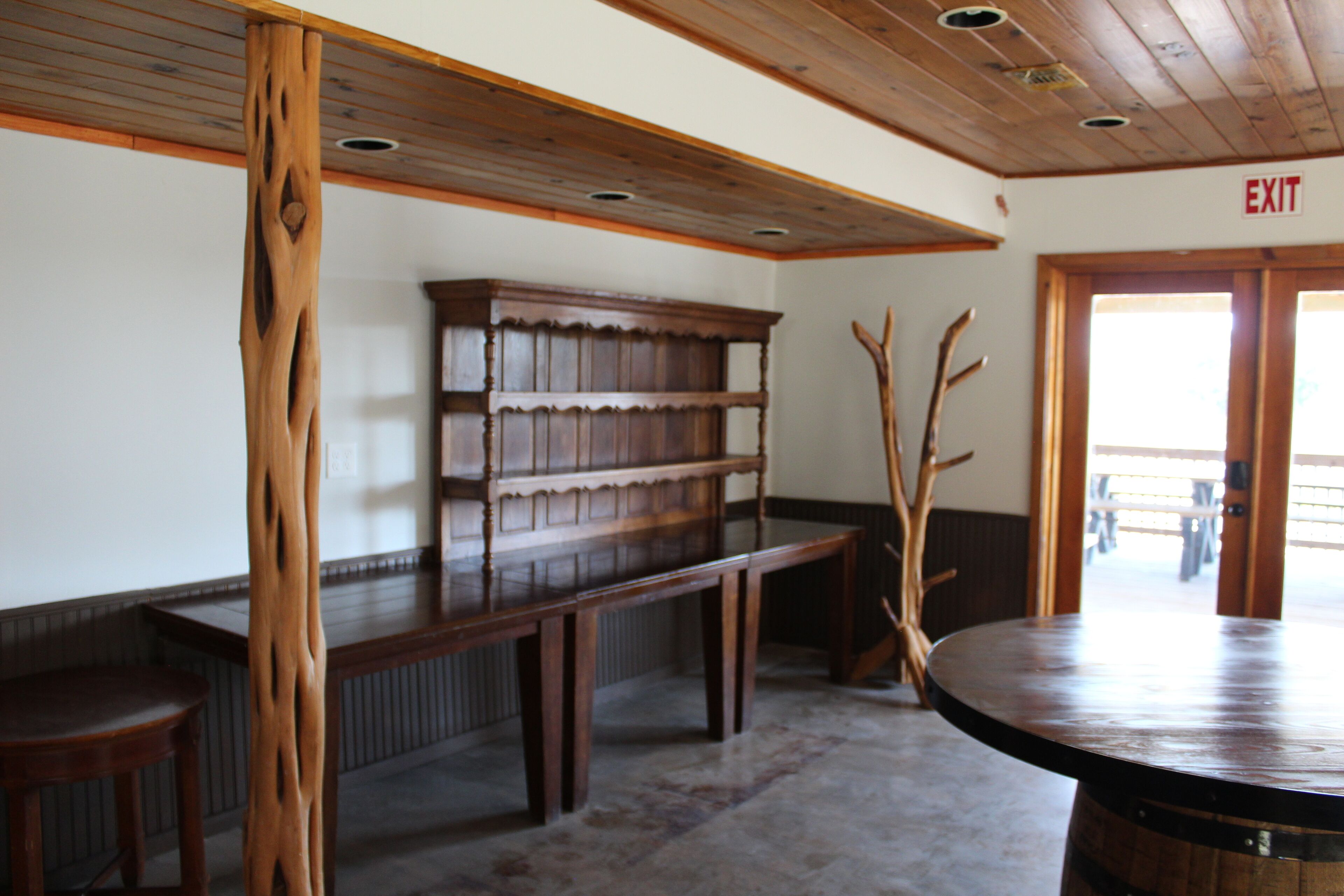 A wooden bench, a bookshelf, and a round table in a room with a wooden ceiling and an exit sign.