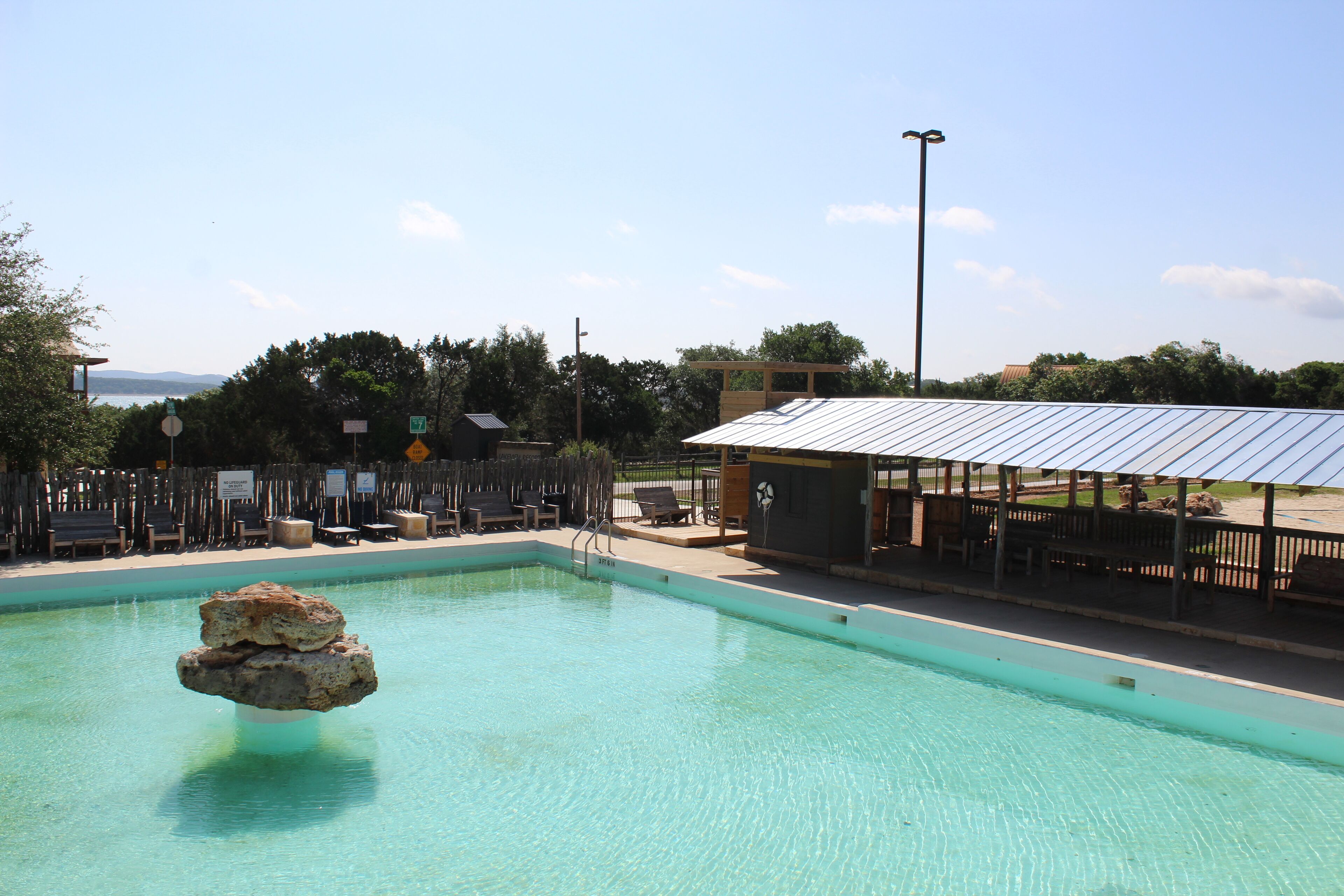 A swimming pool with a rock feature, lounge chairs, and a covered seating area.