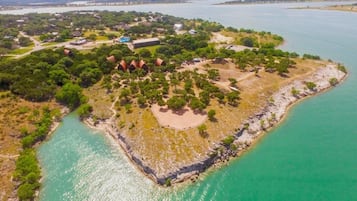 Vista aérea de una propiedad costera con un área verde central, una playa y vegetación circundante.