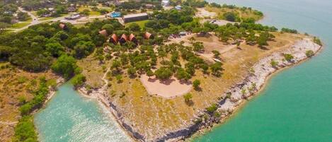 Vista aérea de una propiedad costera con un área verde central, una playa y vegetación circundante.