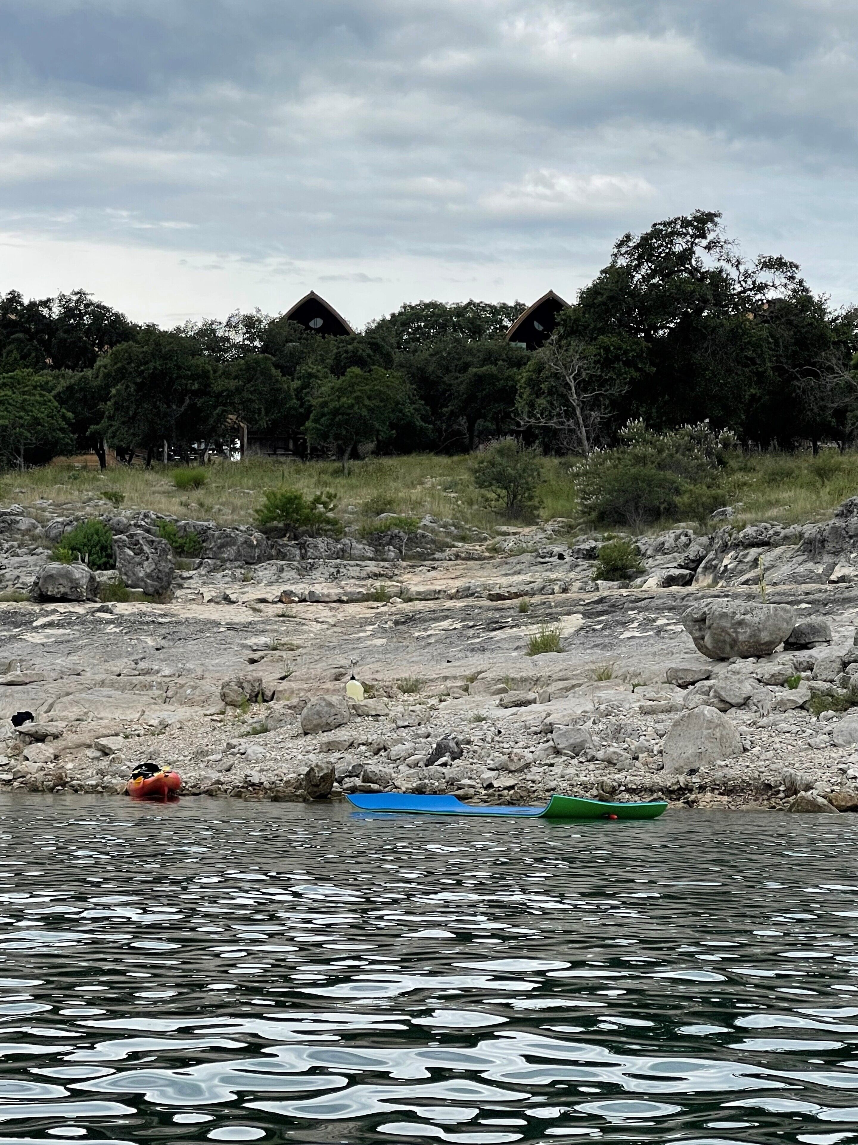 A rocky riverbank with a few boats, trees, and a cloudy sky.