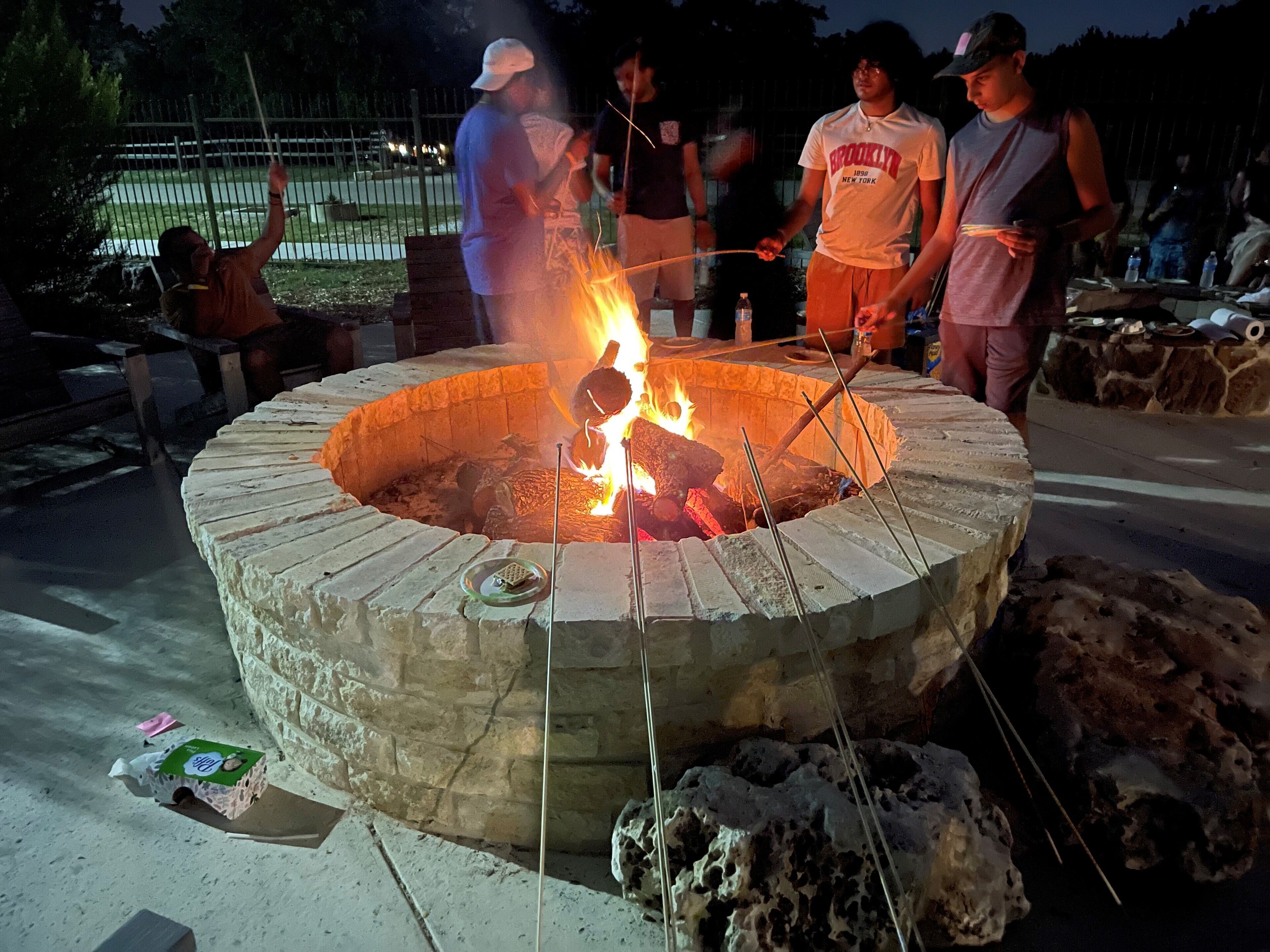 A circular stone fire pit with a fire burning inside, surrounded by people.