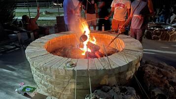 A circular stone fire pit with a fire burning inside, surrounded by people.