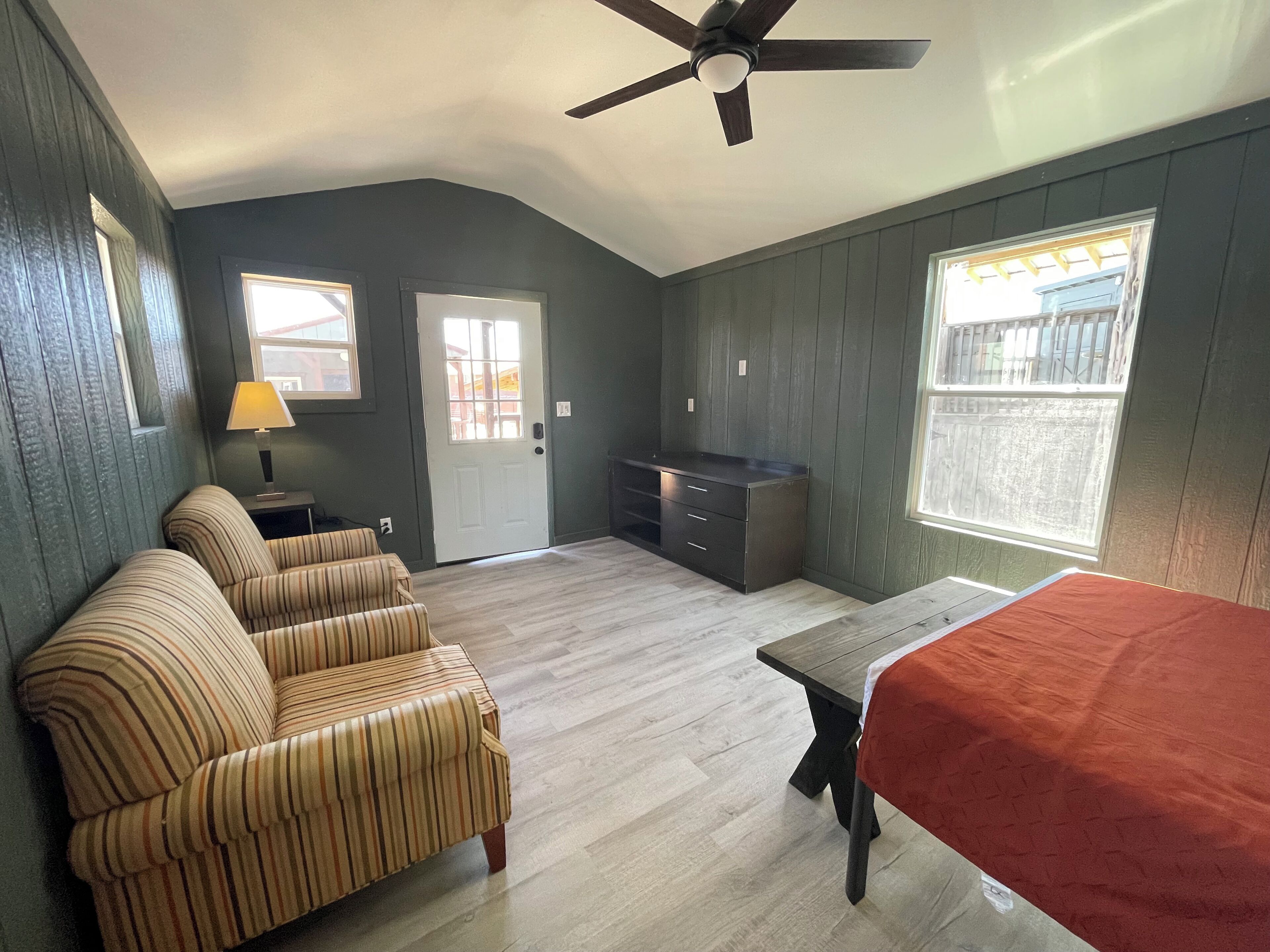 A room with a ceiling fan, a sofa, a table, a cabinet, and a window.
