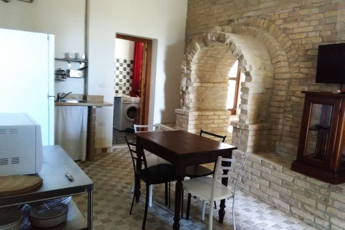 A compact kitchen with a washing machine, a dining table with chairs, and a stone archway leading to a bathroom.