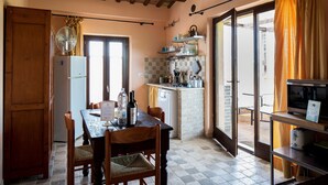 A kitchen with a dining table, chairs, a refrigerator, a sink, and a window with curtains. - Casali Costadoro (Acquaviva Picena)