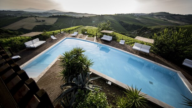 A swimming pool with lounge chairs and a view of rolling hills. - Casali Costadoro (Acquaviva Picena)