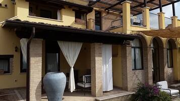A two-story building with a covered patio area, featuring a large vase and a chair.