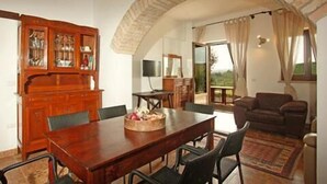 A dining area with a wooden table and chairs, a cabinet with glass doors, and a view of the outdoors through a large window. - Casali Costadoro (Acquaviva Picena)