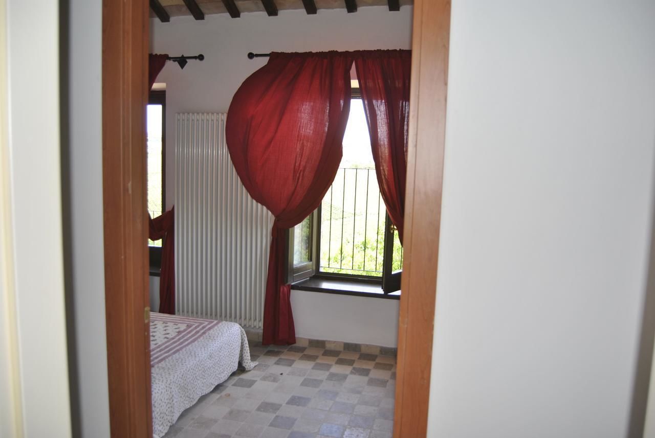 Una habitació amb terra de petxines, un llit amb mantell estampat, una finestra amb vista a vegetació i cortines vermelles.