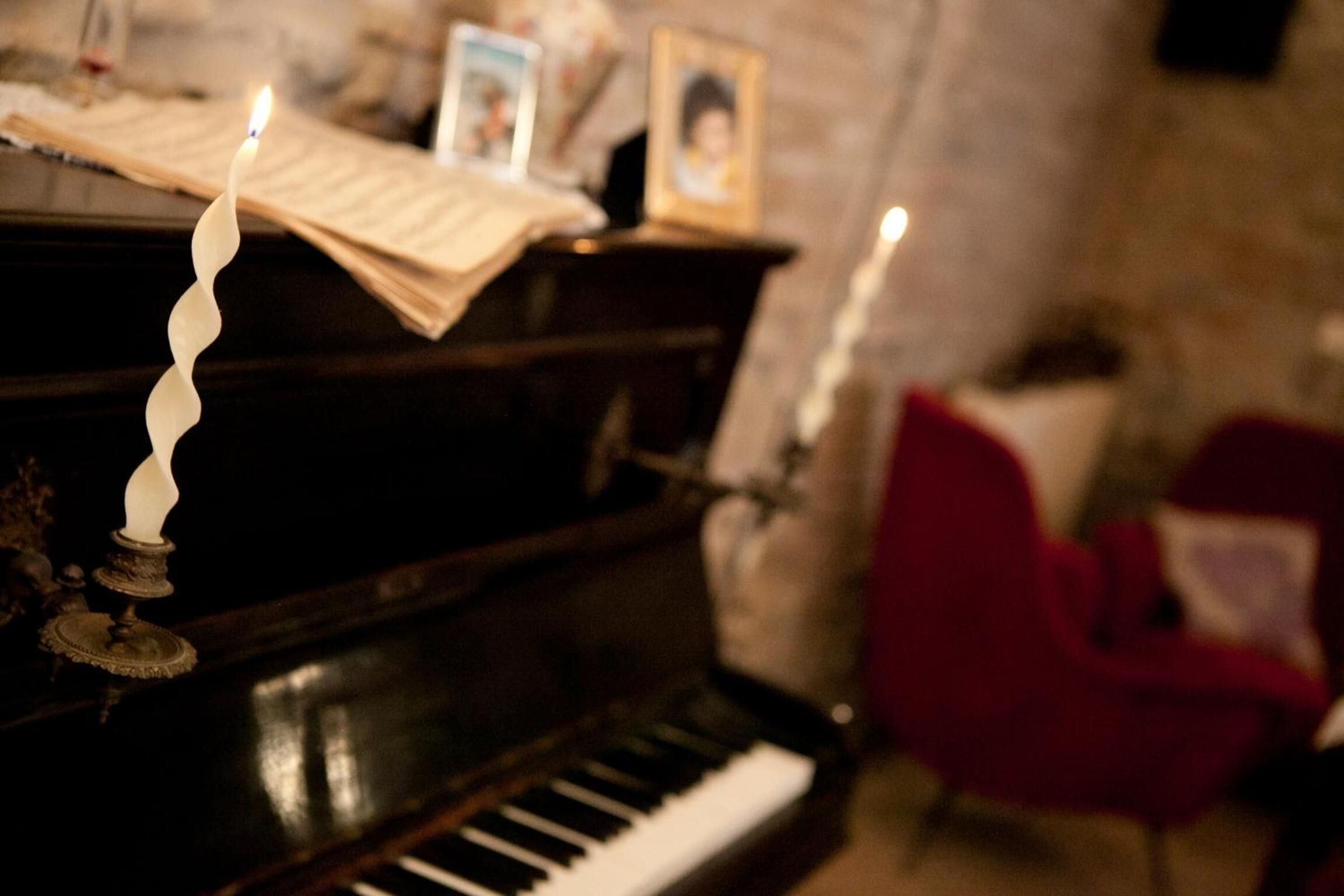 A piano with sheet music, a candle, and framed photos on top.