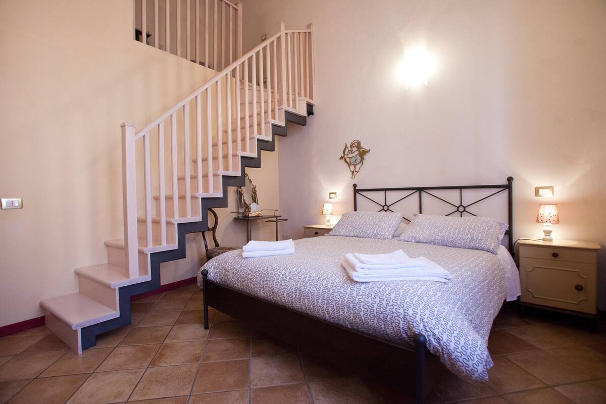 Un dormitorio con una cama, una mesita de noche, una lámpara, un reloj de pared y una escalera.