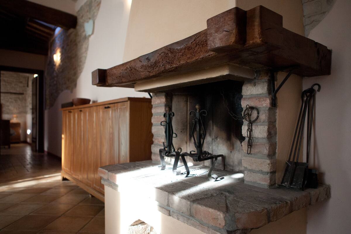 Una chimenea de piedra con repisa de madera y ganchos metálicos para colgar objetos.
