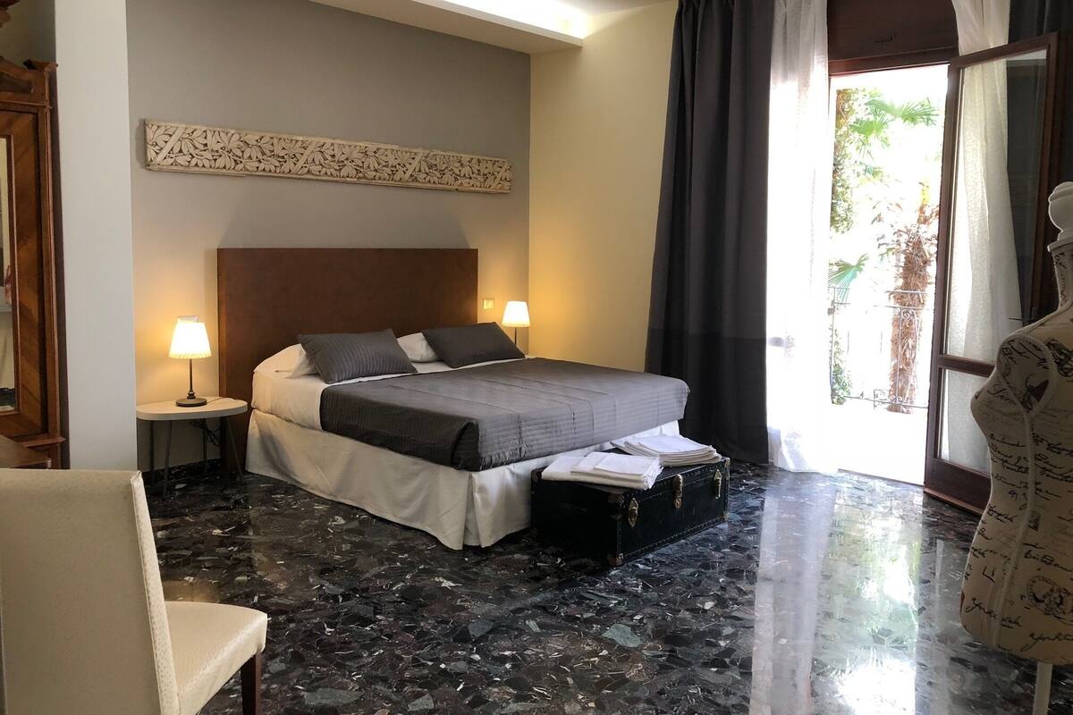 Habitación de hotel con una cama, dos lámparas de noche, un adorno en la pared, una maleta y una silla.