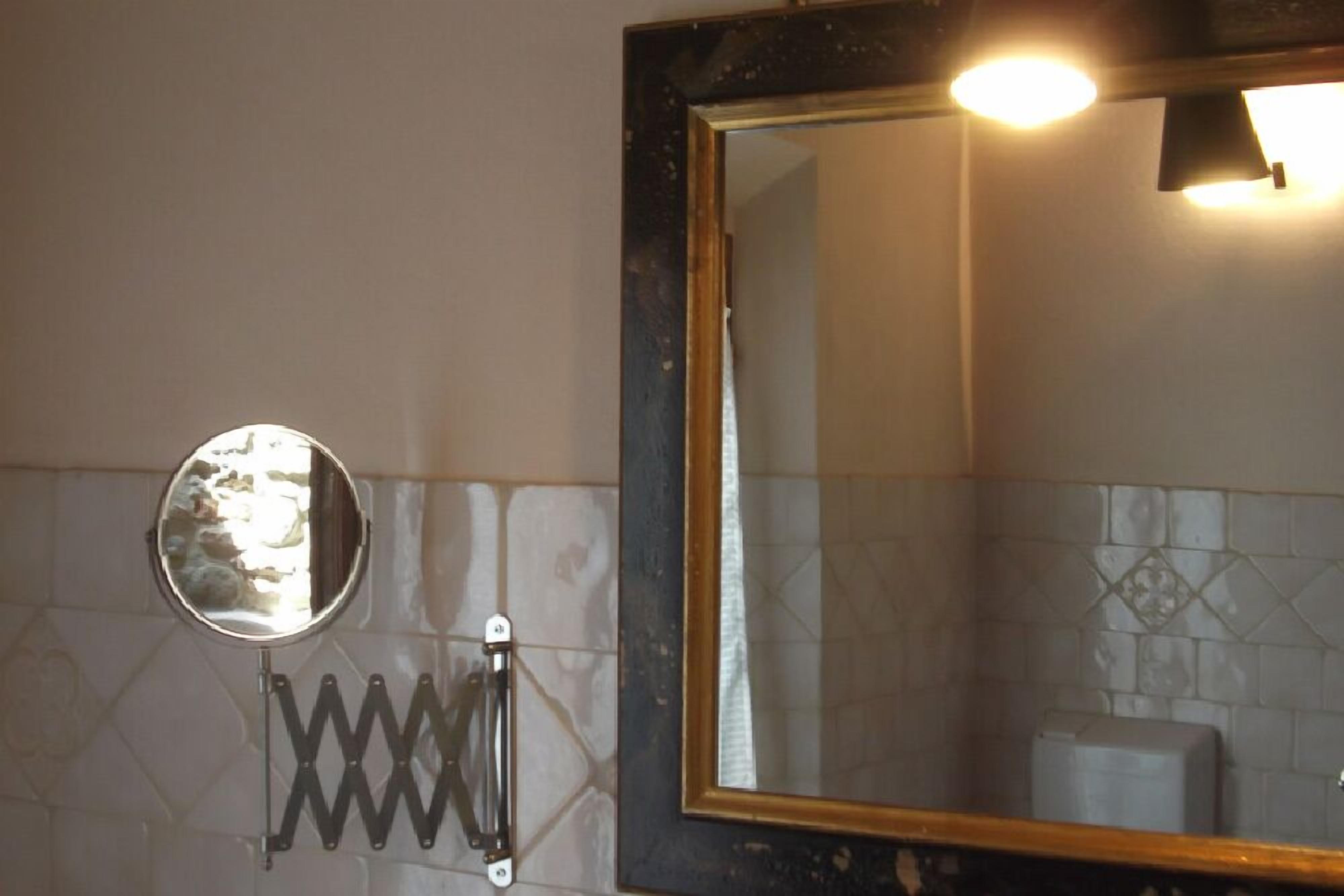 Une salle de bain avec un grand miroir, un miroir rond et un porte-serviettes.