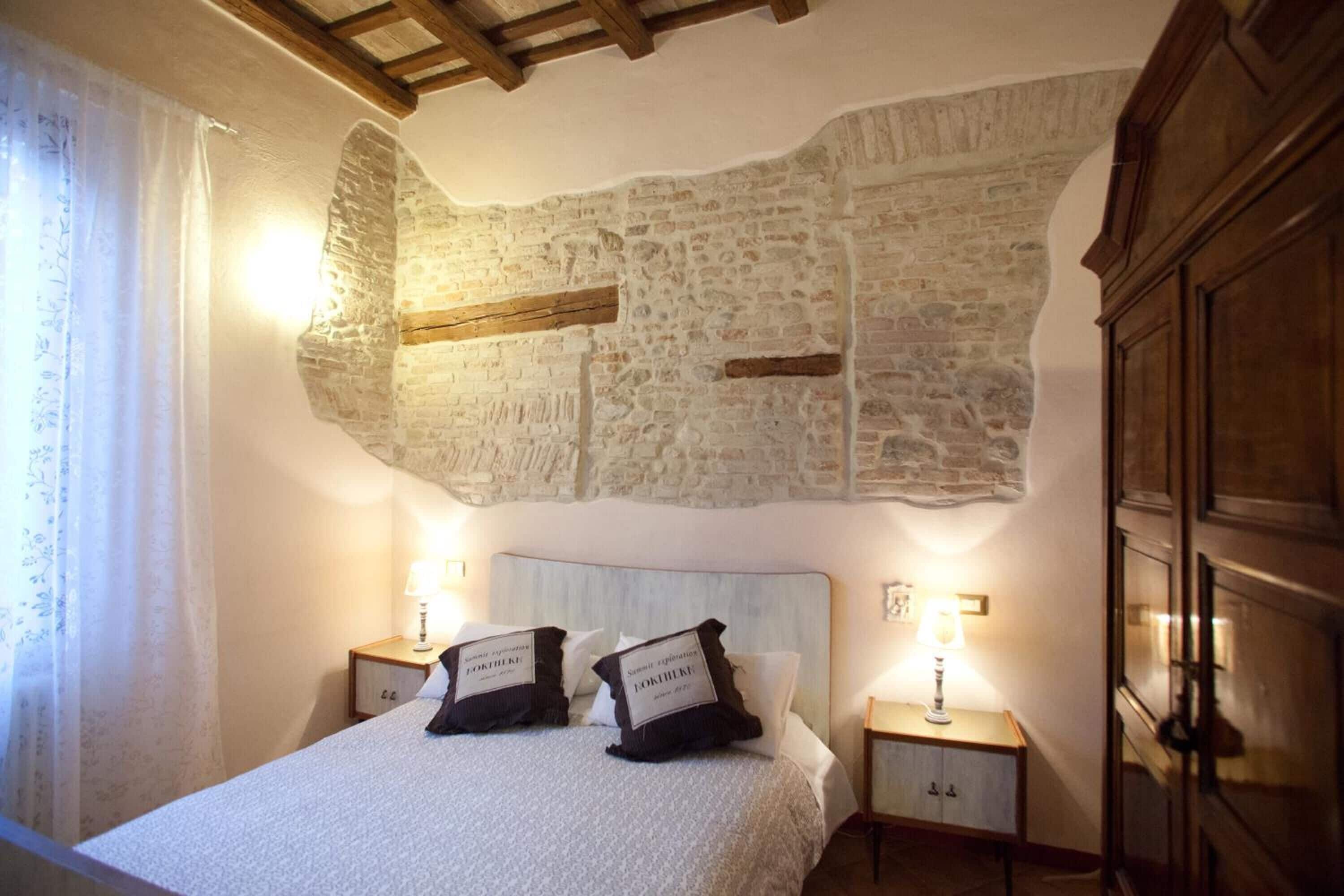 Een slaapkamer met een stenen muur, een bed met twee kussens en twee nachtkastjes met lampen.