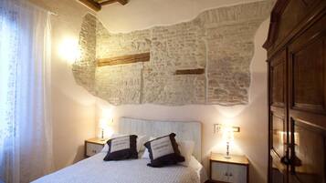 A bedroom with a stone wall, a bed with two pillows, and two bedside tables with lamps.
