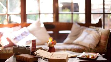 A cozy room with a wooden table, books, a lamp, and a window with a view of greenery.