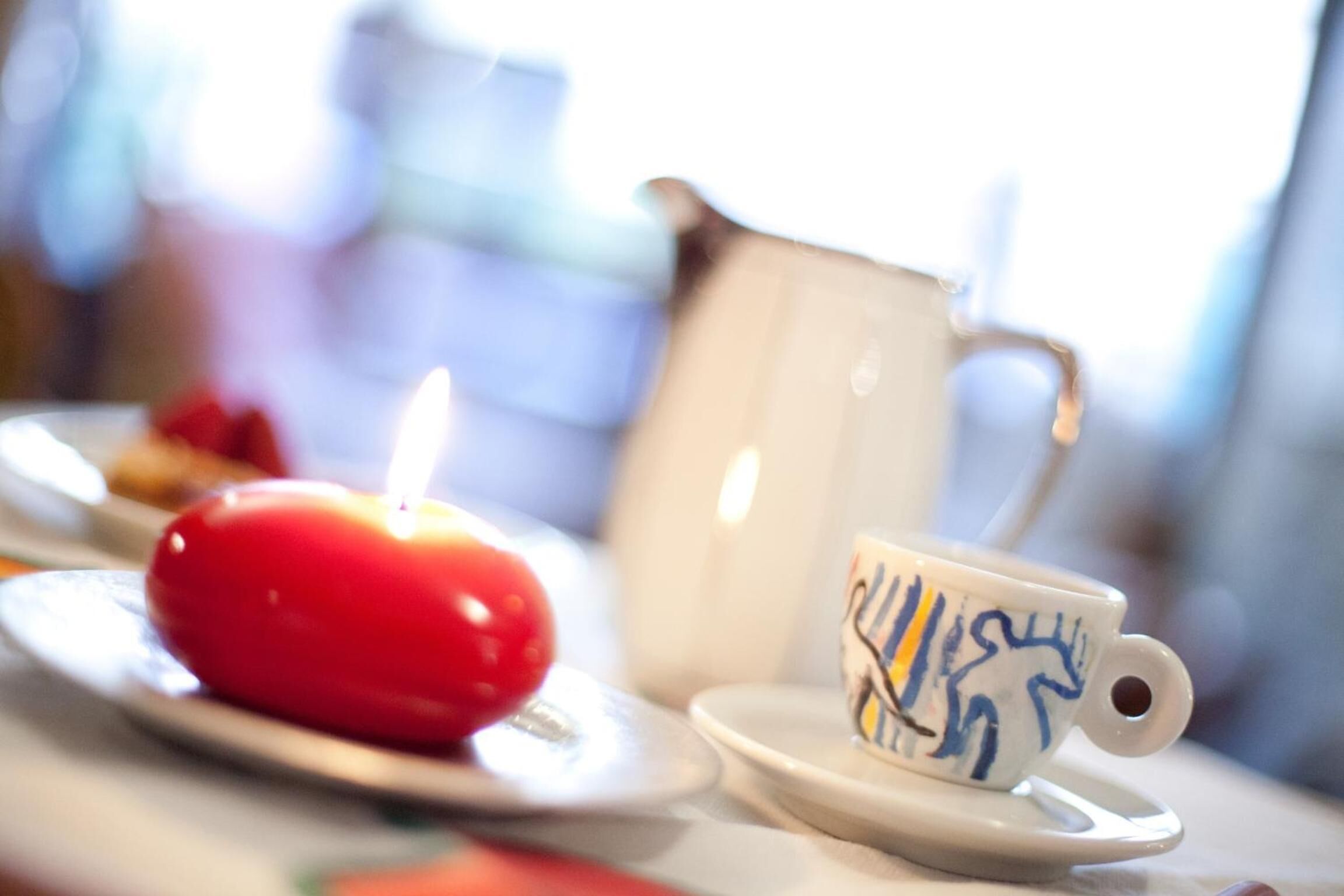 Une table avec une bougie rouge, une tasse en céramique à motifs bleus et un pichet blanc.