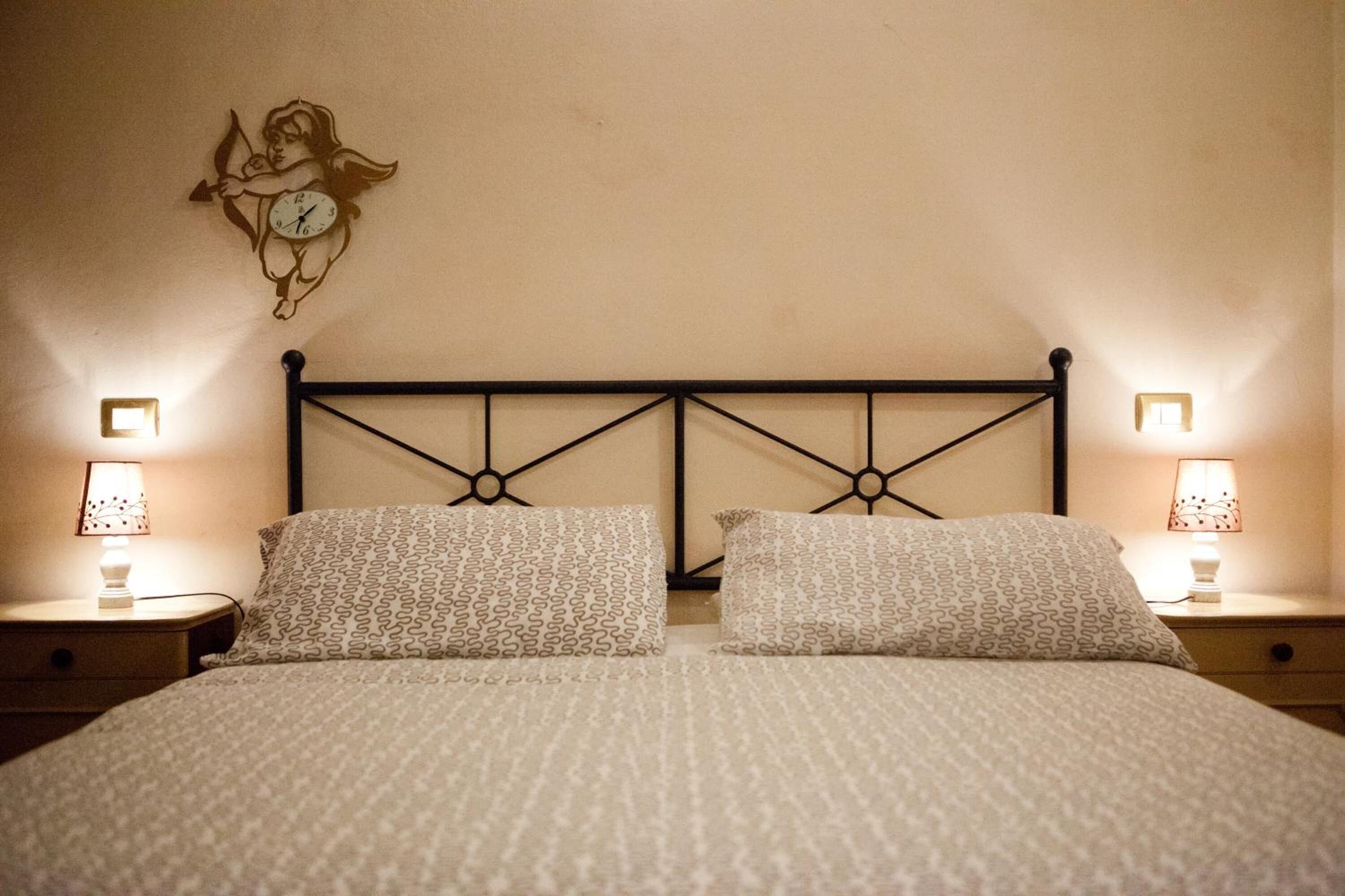 A neatly made bed with patterned pillows and a wall clock. There are two bedside lamps on either side of the bed.
