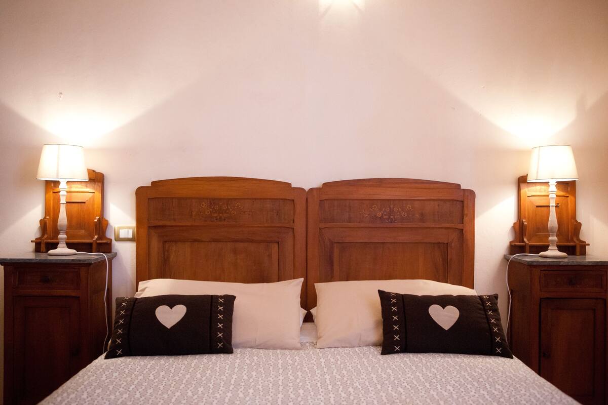 Una cama doble con cabecera de madera, dos lámparas de noche y almohadas con forma de corazón.