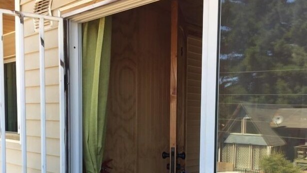 Una puerta corredera de vidrio con marco de madera, una cortina verde y un extintor colgado en la pared.