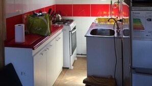 Una cocina pequeña con armarios blancos, salpicadero rojo, una ventana y un refrigerador.