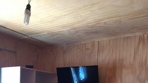Una habitación con pared revestida de madera, un televisor de pantalla plana montado sobre una unidad de almacenamiento empotrada, y una cama con manta rosa.