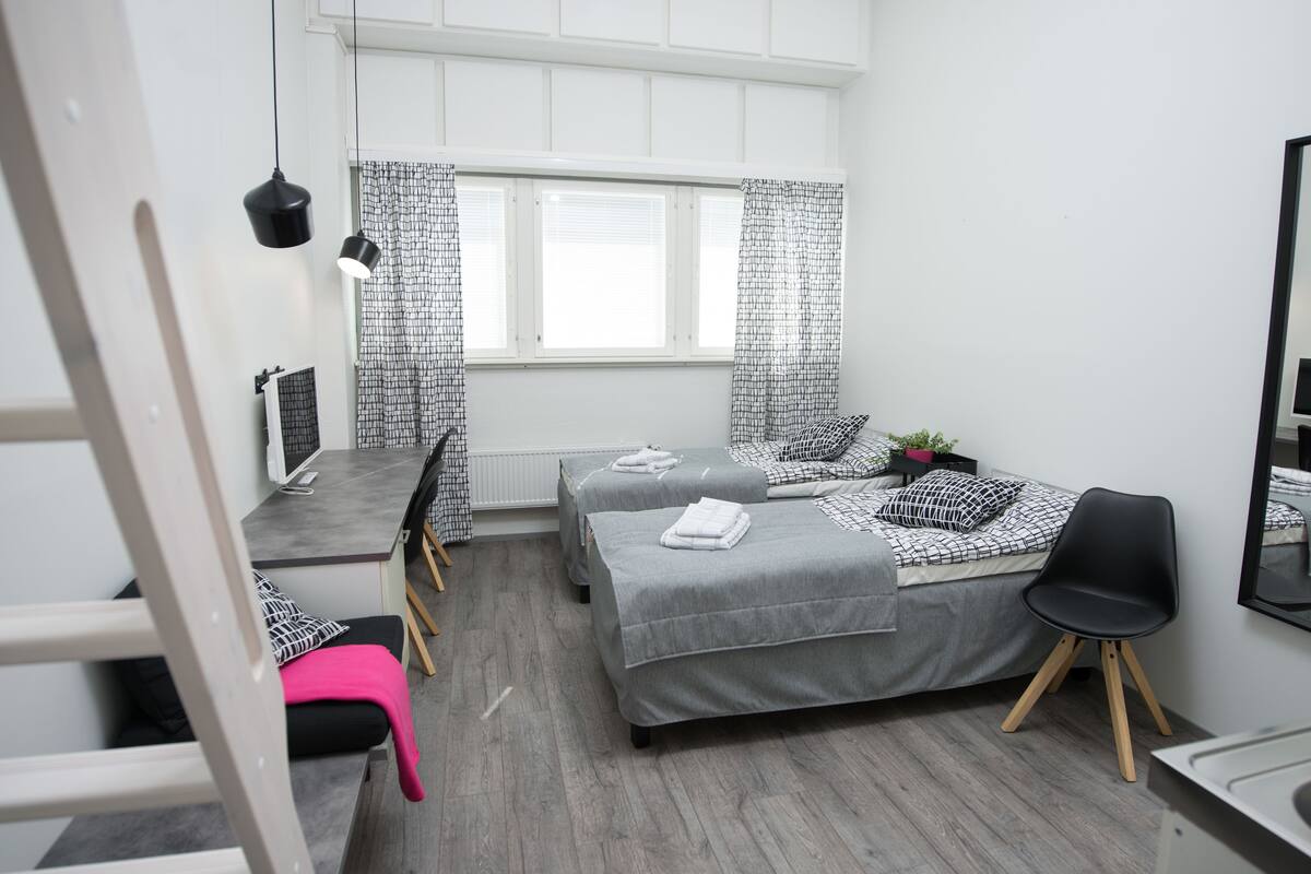 A small, modern bedroom with a bed, two bedside tables, a chair, and a window with curtains.