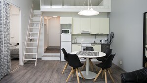 A compact kitchen with white cabinets, a microwave, and a coffee maker. There's a dining area with a round table and four chairs. A white ladder leads to a lofted sleeping area. - Innotelli Apartments (Helsinki)