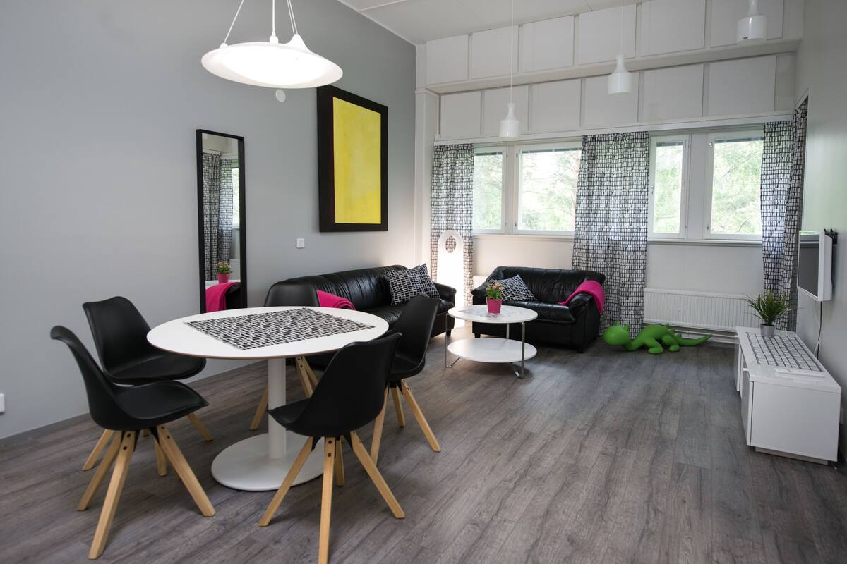 A modern living room with a dining table, black chairs, a sofa, and a window with patterned curtains.