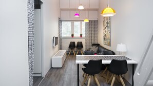 A modern kitchen with a white countertop, black chairs, and a white table. There are three pendant lights above the table. - Innotelli Apartments (Helsinki)