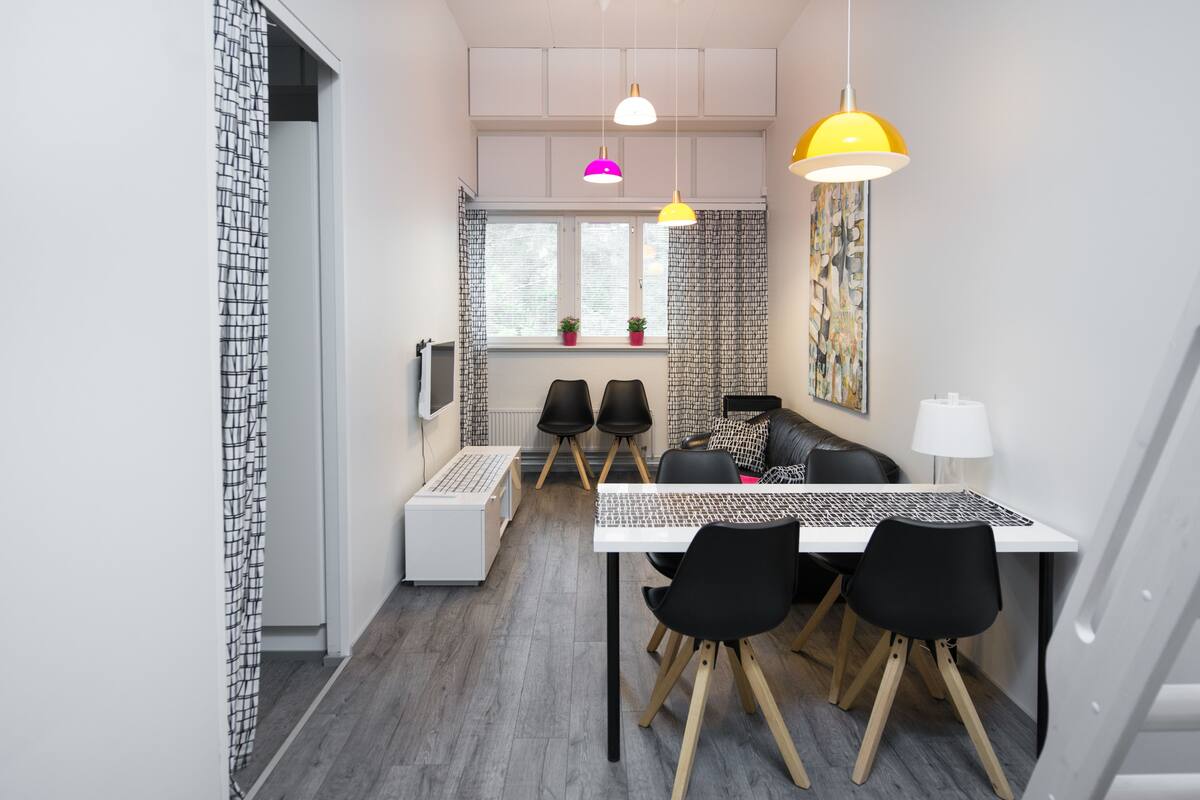A modern kitchen with a white countertop, black chairs, and a white table. There are three pendant lights above the table.