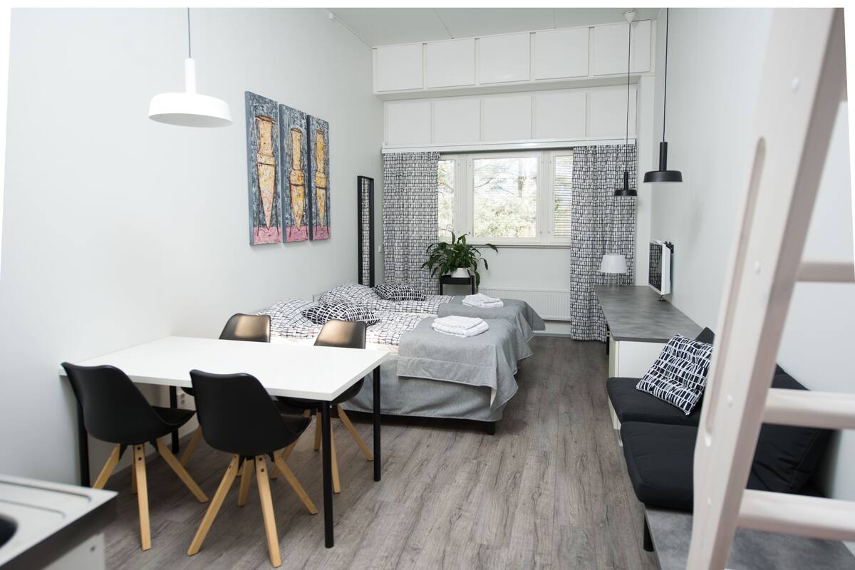 A compact room with a dining table, two beds, a potted plant, and artwork on the walls.