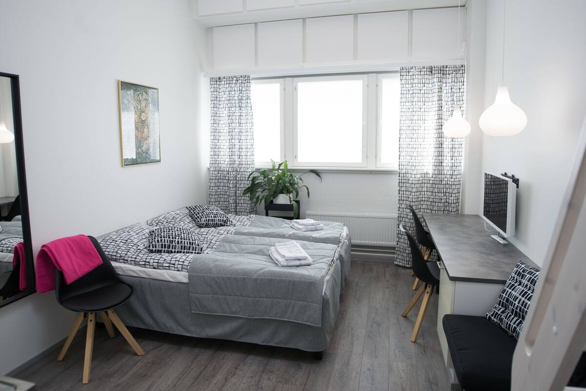 A modern bedroom with a bed, desk, and chair, a potted plant, and a window with curtains.